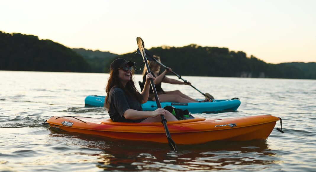 woman in blue shirt and blue denim jeans riding orange kayak on water during daytime